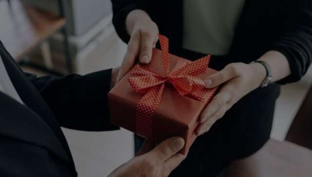 Gifts and hospitality compliance - Female employee receiving a red gift box from a client in an office.